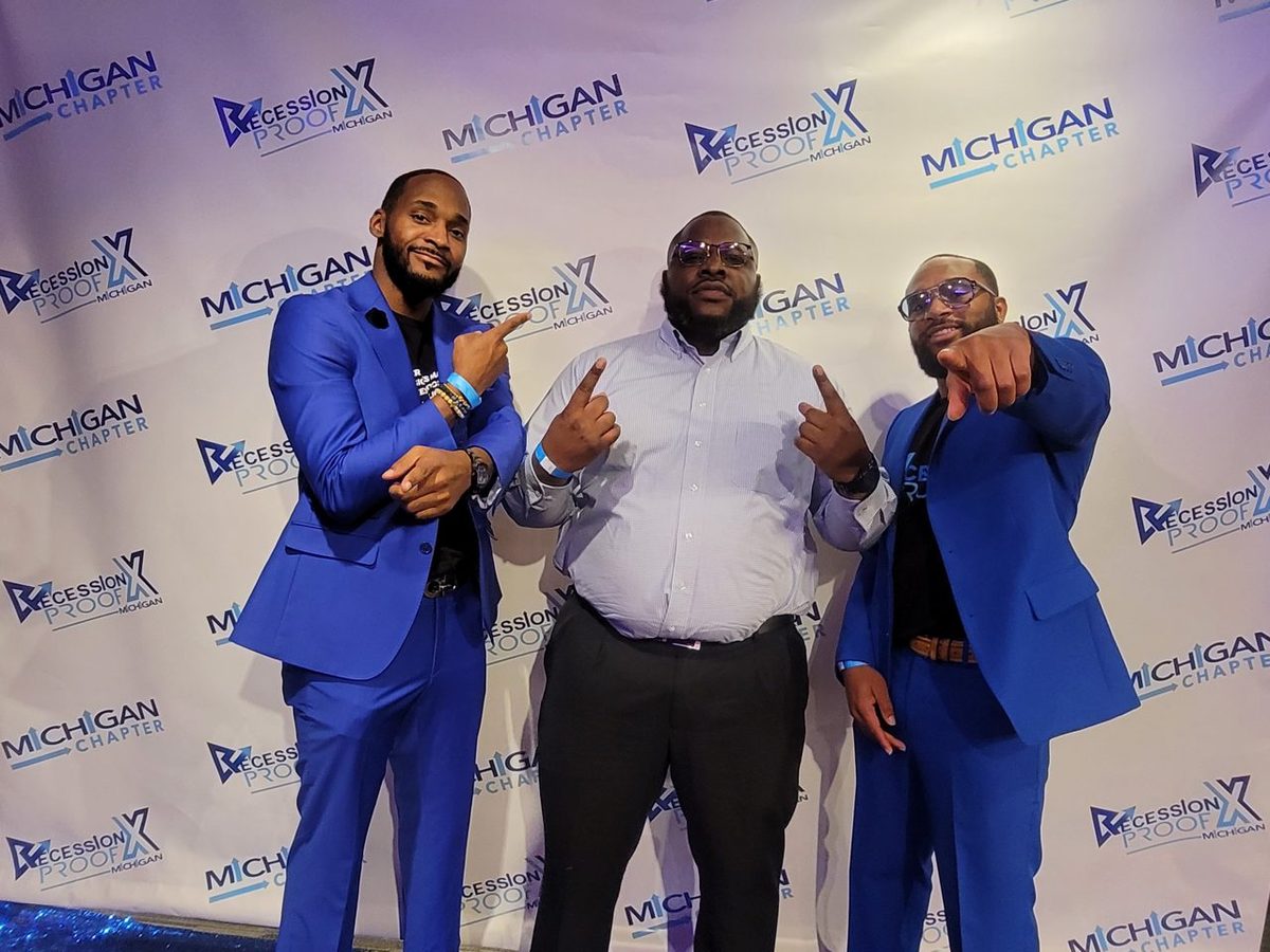 Three chapter leaders in blue suits at the Recession Proof Michigan backdrop.